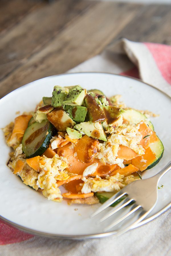 Avocado and Spiralized Sweet Potato Hash with Zucchini on a white plate with linen napkin.